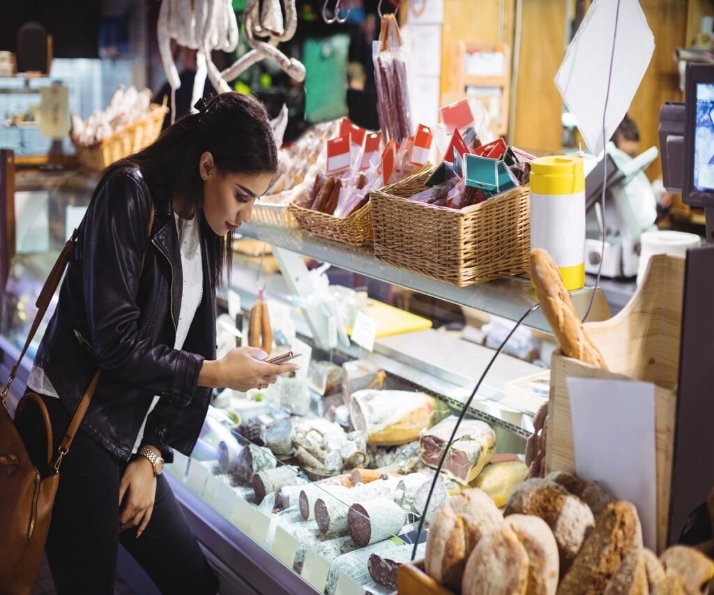 Woman using mobile phone while looking at food display in supermarket