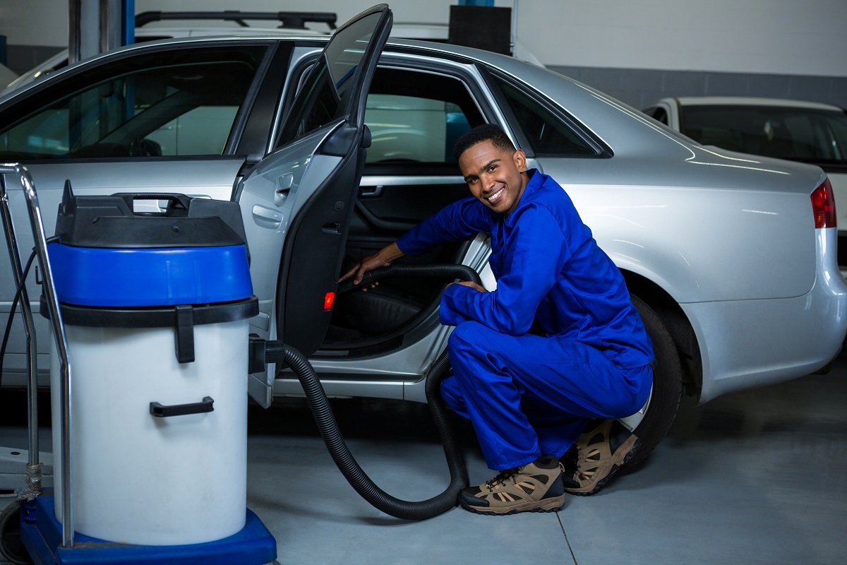 Portrait of mechanic servicing car with vacuum cleaner