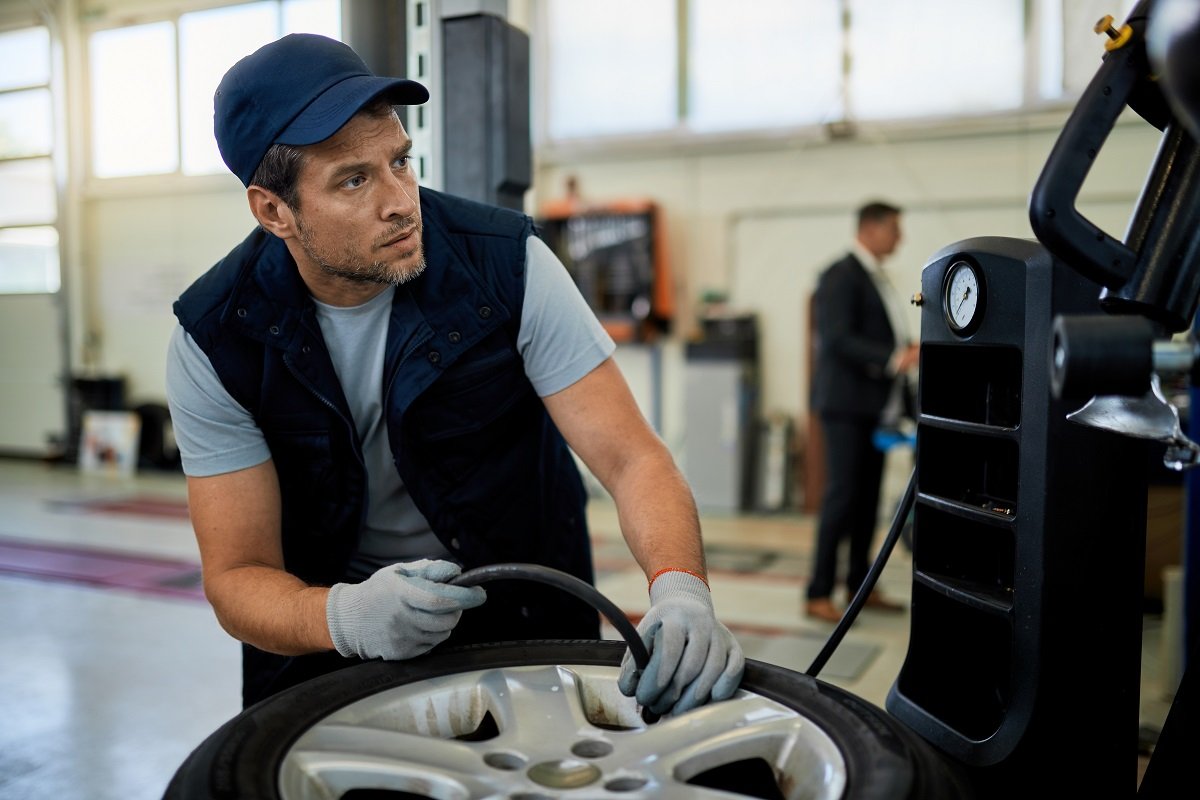 Car mechanic adjusting tire pressure while working at auto repair shop.